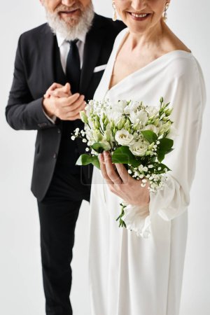 Middle aged man in tuxedo and woman in white wedding dress embracing in a studio setting, celebrating their special day.