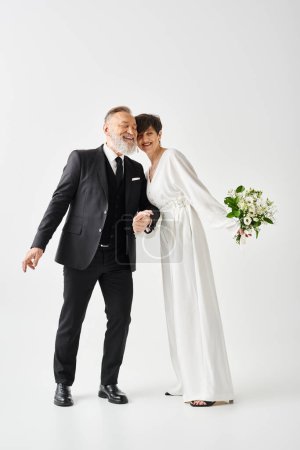 Middle-aged bride and groom, dressed in wedding gowns, strike a pose in a studio setting to capture their special day.