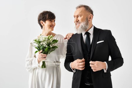 A middle-aged bride and groom celebrate their special day in a studio, the man in a tuxedo and the woman in a white dress.