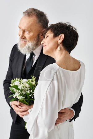 A middle aged bride and groom in wedding attire embrace joyfully in a studio setting, celebrating their special day together.