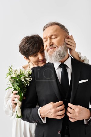 Middle-aged bride and groom in elegant wedding attire embrace each other on their special day in a studio setting.