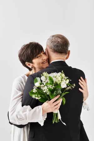 A middle-aged bride and groom in wedding gowns share a heartfelt hug to celebrate their special day in a studio setting.