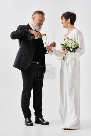 Middle-aged bride and groom in wedding gowns holding champagne glasses, celebrating their special day in a studio setting.