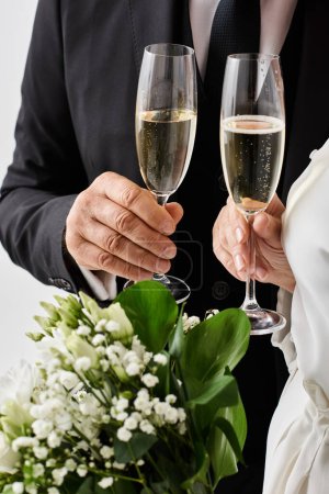 Middle-aged bride and groom in wedding attire happily raise champagne flutes in celebration.