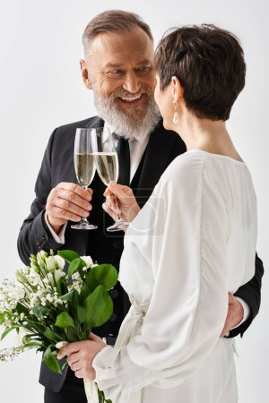 Braut und Bräutigam mittleren Alters in Hochzeitskleidung klappern Champagnergläser in einem Studio-Ambiente und feiern ihren besonderen Tag.