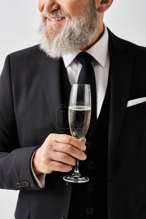 Bräutigam mittleren Alters im eleganten Anzug, der anmutig ein Champagnerglas in der Hand hält und an seinem Hochzeitstag Raffinesse und Klasse ausstrahlt.