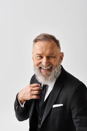 Photo for A middle-aged groom is adjusting his tie while smiling in an elegant tuxedo on his wedding day in a studio setting. - Royalty Free Image