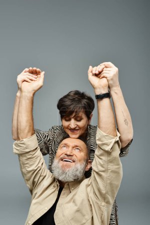 Un homme d'âge moyen en tenue élégante tient une femme sur ses épaules dans un cadre de studio, montrant force et affection.