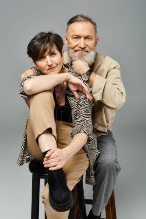 Mann und Frau mittleren Alters in modischer Kleidung sitzen auf einem Hocker in einem Studio-Setting.