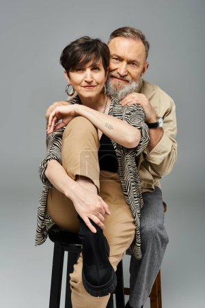 Ein Mann und eine Frau mittleren Alters sitzen auf einem Schemel in einem stilvollen Studio-Ambiente, unterhalten sich und unterhalten sich..