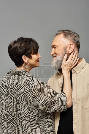 Foto de Un hombre y una mujer de mediana edad con un atuendo elegante se paran elegantemente uno al lado del otro en un entorno de estudio. - Imagen libre de derechos