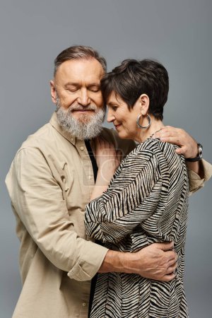 Un hombre y una mujer de mediana edad con un atuendo elegante abrazándose firmemente en un entorno de estudio, expresando amor y conexión.
