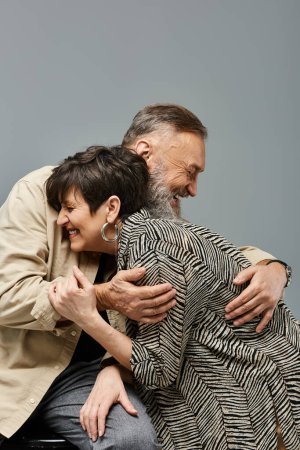A middle-aged man lovingly hugs a woman from behind on the back of a chair in a stylish studio setting.