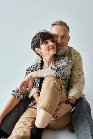 Photo for Stylish middle-aged couple seated closely, exuding charm and sophistication in a studio setting. - Royalty Free Image
