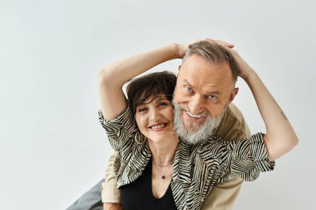 A middle-aged man and woman, stylishly dressed, strike a pose together in a studio setting.