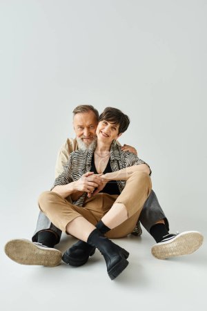 A middle-aged couple dressed in stylish attire sitting on the ground in a studio setting.