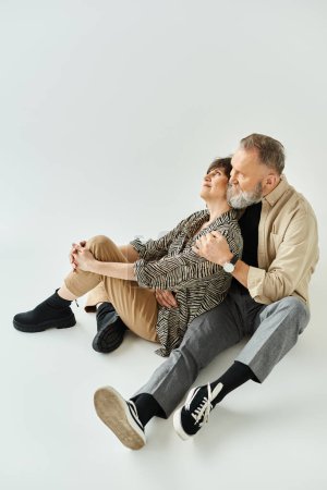 A middle aged man and woman in stylish attire sitting together on the ground in a serene pose.