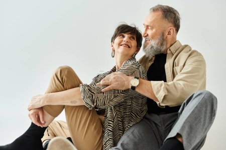 Téléchargez les photos : Un couple d'âge moyen en tenue élégante assis près du sol dans un cadre studio, partageant un moment de paix et de connexion. - en image libre de droit