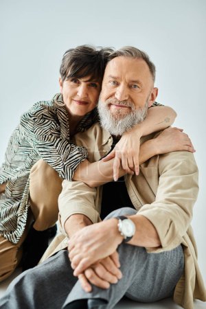 A middle-aged couple in stylish attire share a heartfelt hug, expressing love and connection in a studio setting.
