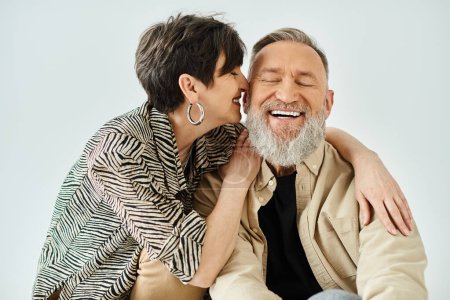 Photo for A middle-aged couple in stylish attire sitting closely together, exuding elegance and warmth in a studio setting. - Royalty Free Image