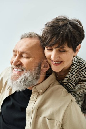 Un hombre y una mujer de mediana edad con un atuendo elegante, sonriendo calurosamente el uno al otro en un entorno de estudio.