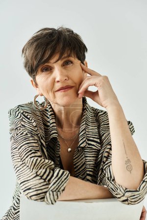 Foto de Una mujer de mediana edad con el pelo corto, sentada en una mesa, profundamente pensada con la mano apoyada en la cabeza. - Imagen libre de derechos