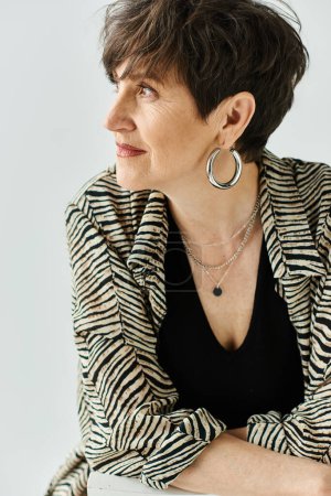 A middle-aged woman with short hair stunningly styled in a black top paired with a fashionable zebra print jacket in a studio setting.