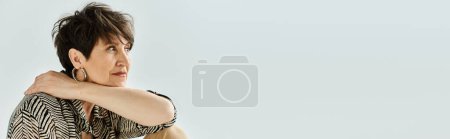 Foto de Mujer de mediana edad con pelo corto, vestida con un atuendo elegante, posando con confianza con los brazos cruzados en un entorno de estudio. - Imagen libre de derechos