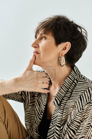 A middle-aged woman with short hair and stylish attire sitting down, deep in thought with her hand on her chin.