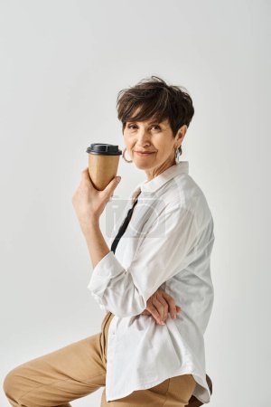 Una mujer de mediana edad con cabello corto y atuendo elegante posa con gracia mientras sostiene una taza de café.