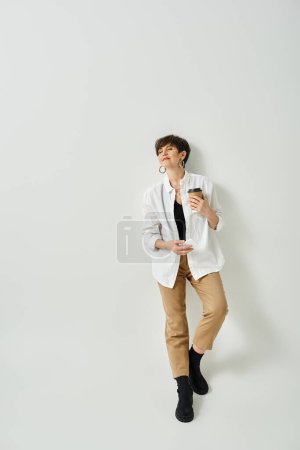 Photo for A middle-aged woman with short hair stands in front of a white wall in a stylish attire, exuding elegance and confidence. - Royalty Free Image