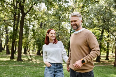An adult loving couple in casual attire leisurely walking through a park.