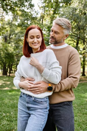 Téléchargez les photos : Un couple aimant les adultes en tenue décontractée debout dans le parc herbeux. - en image libre de droit