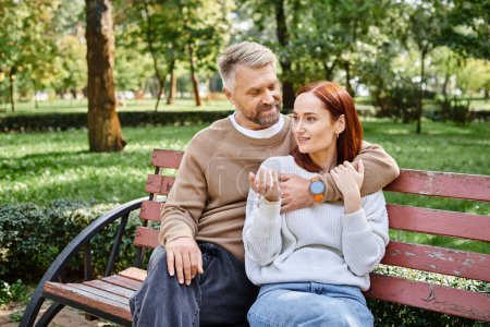 Téléchargez les photos : Un homme et une femme en tenue décontractée s'assoient ensemble sur un banc de parc, profitant mutuellement de la compagnie. - en image libre de droit