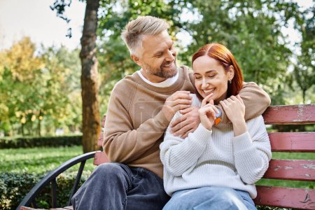 Téléchargez les photos : Couple aimant adulte en tenue décontractée se relaxant sur un banc de parc. - en image libre de droit