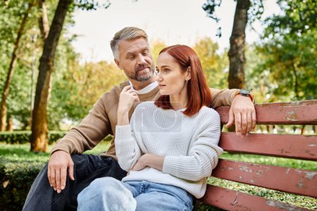 Téléchargez les photos : Un homme et une femme en tenue décontractée assis paisiblement ensemble sur un banc de parc. - en image libre de droit