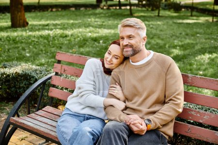 A loving couple in casual attire sitting together on a bench in a peaceful park setting.