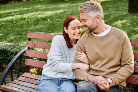 Un homme et une femme en tenue décontractée s'assoient ensemble sur un banc en bois dans un parc.