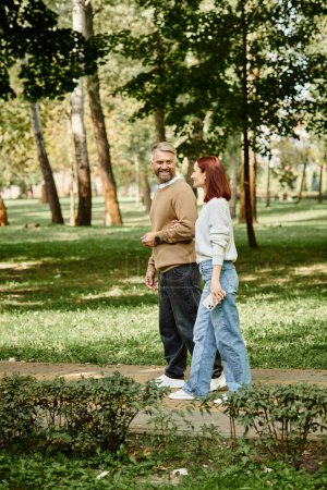 A man and a woman, a loving couple, strolling through a park in casual attire.