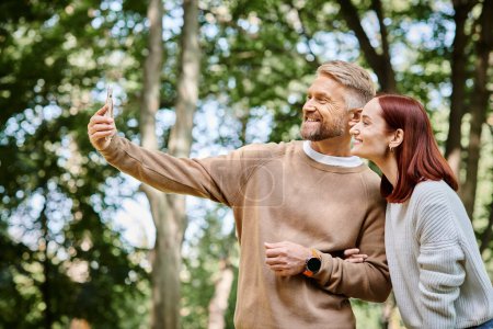 A man and woman capture a moment in the park with a cell phone.