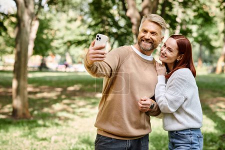 A man and woman capture a moment together in a park by taking a selfie.