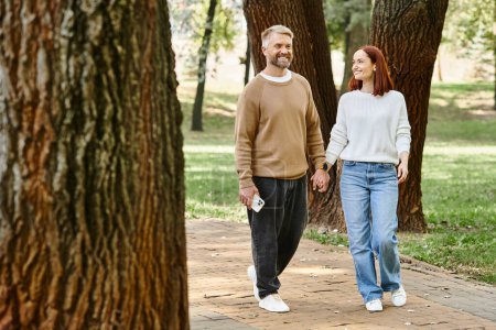Ein Mann und eine Frau in Freizeitkleidung gehen gemeinsam in einem friedlichen Park spazieren.
