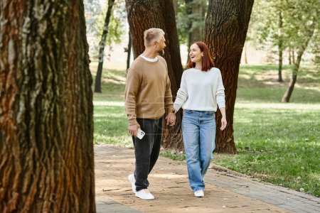 Foto de Una pareja, casualmente vestida, camina de la mano en un parque. - Imagen libre de derechos