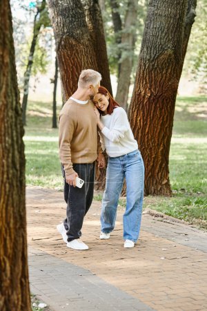 Foto de Un hombre y una mujer en atuendo casual se paran juntos en un parque, rodeados de naturaleza. - Imagen libre de derechos