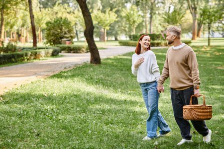 Téléchargez les photos : A couple leisurely walks through a park surrounded by lush greenery. - en image libre de droit