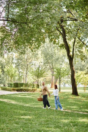 Una pareja cariñosa, casualmente vestida, camina por un parque tranquilo.