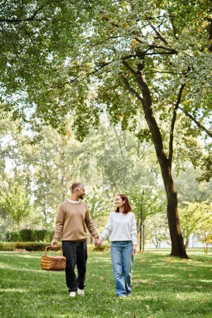 Photo for Man and woman in casual attire holding hands, walking through park. - Royalty Free Image