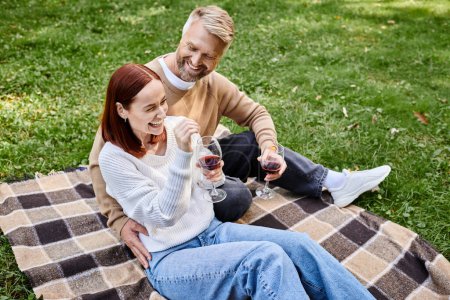 Téléchargez les photos : Un homme et une femme assis ensemble sur une couverture, tenant des verres à vin. - en image libre de droit
