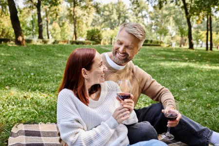 Hombre y mujer sentados en una manta, sosteniendo copas de vino, disfrutando de un momento romántico al aire libre.