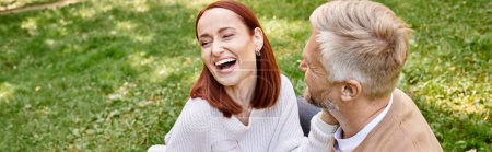 A man and a woman happily laugh while enjoying each others company in a grassy field.